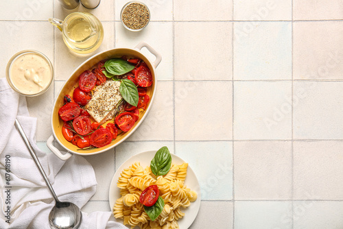 Baking dish with tasty tomatoes  feta cheese and pasta on white tile background