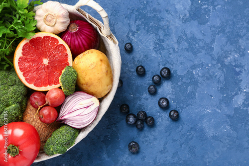 Fototapeta Naklejka Na Ścianę i Meble -  Wicker basket with different fresh fruits and vegetables on blue background, closeup