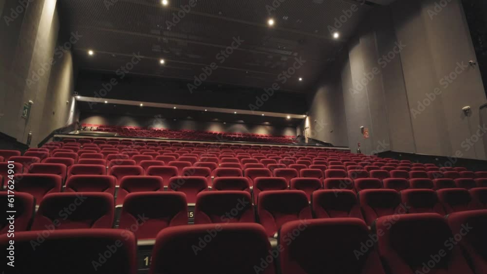 Slow dolly shot along rows of red cinema seats with bright lights