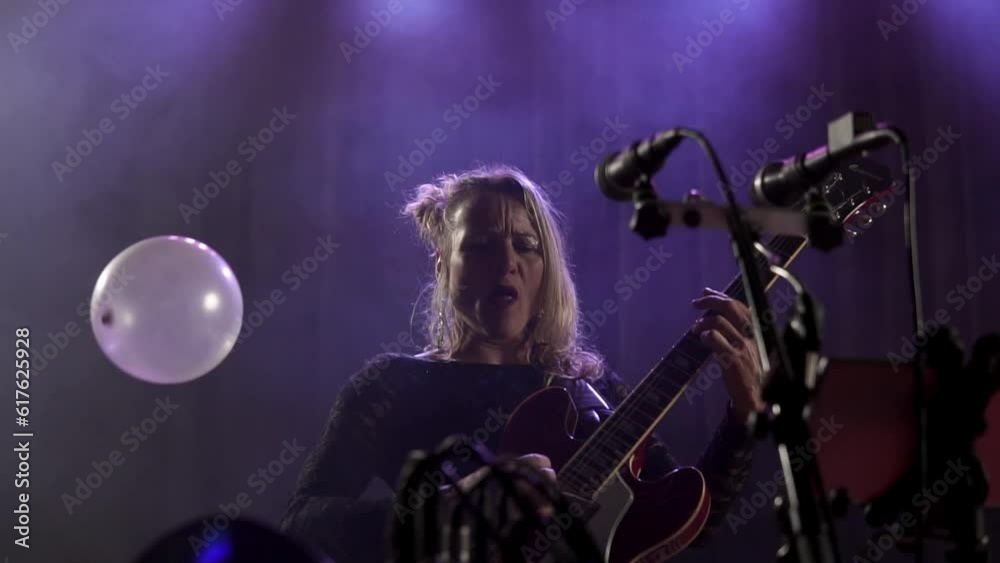 Silhouette of a professional woman vocalist performing in night club lights with guitar close up. Beautiful blonde lady performing a song, holding microphone in stylish clothes. Entertainment concept Silhouette of a professional woman vocalist performing in night club lights with guitar close up. Beautiful blonde lady performing a song, holding microphone in stylish clothes. Entertainment concept