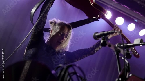 Closeup of an excited Professional guitarist singing, screaming and performing in night club lights close up. Attractive hot girl singer dancing, jumping with guitar, hands in the air and having fun