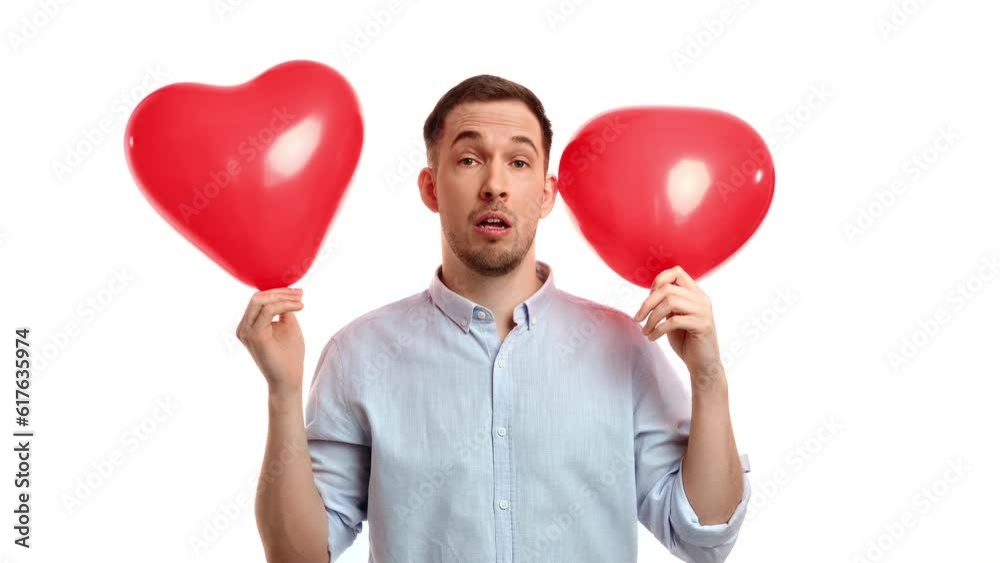 Playful handsome man holding two red heart air balloons having fun with positive emotion isolated Playful handsome man holding two red heart air balloons having fun with positive emotion isolated