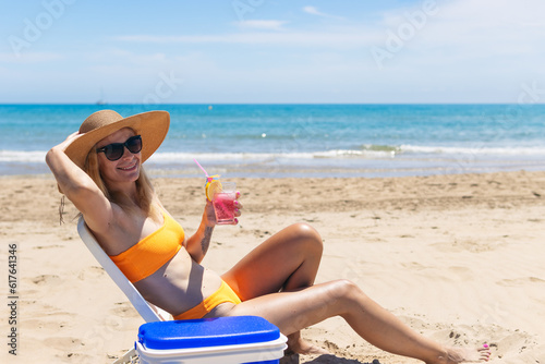 Happy young european girl drinks a cocktail and rests in a sun lounger on the beach, 