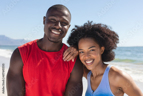 Portrait of happy, fit african american couple embracing and smiling on sunny beach