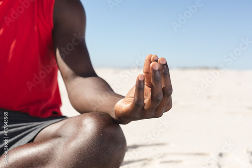 Midsection of fit african american man practicing yoga meditation sitting on sunny beach