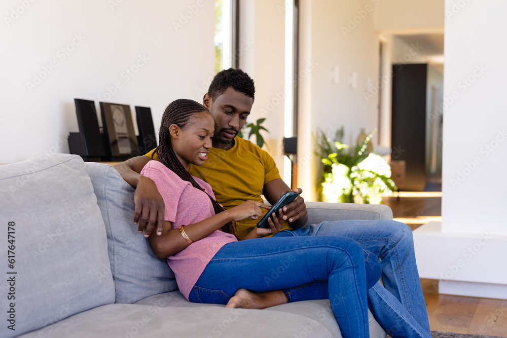 Happy african american couple smiling, embracing and using smartphone on couch at home Happy african american couple smiling, embracing and using smartphone on couch at home