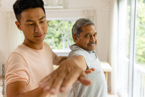 Happy diverse male physiotherapist advising and senior male patient stretching arm