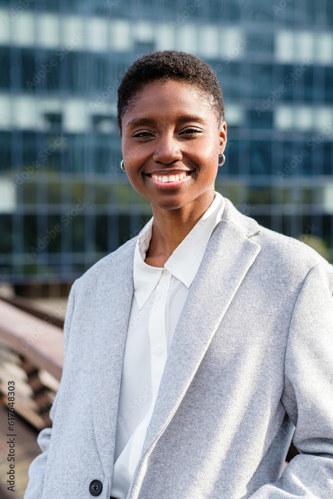 Obraz premium vertical portrait of a young african woman staying on a bridge of financial district. She looks at camera and smiles