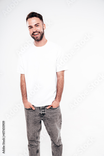Portrait of handsome smiling stylish hipster lambersexual model. Sexy man dressed in white T-shirt and jeans. Fashion male isolated on white background in studio