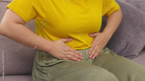 Stomach pain, hands and woman on a sofa with pms, cramps or gas, menstruation or bloating in her home. Tummy, ache and female person with endometriosis, fibroids and colon or constipation problem photo