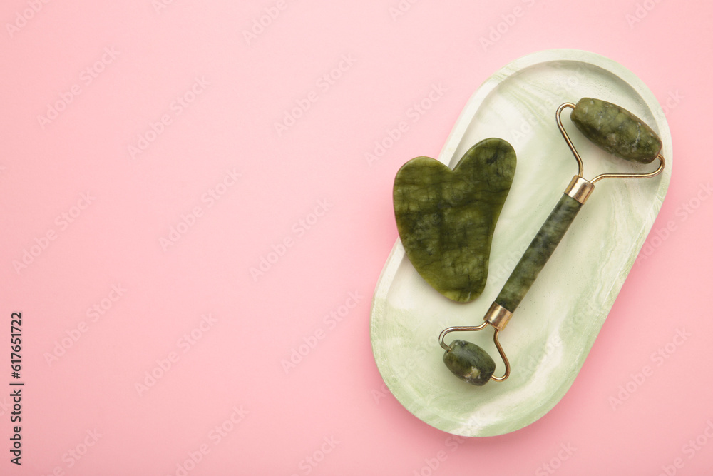 Face massage roller and gouache on plaster tray on pink background. Concept of self and beauty care. Face massage roller and gouache on plaster tray on pink background. Concept of self and beauty care.