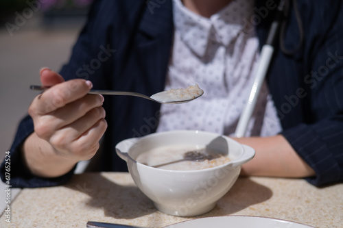 Blind caucasian woman in suit eating porridge for breakfast in outdoor cafe. 