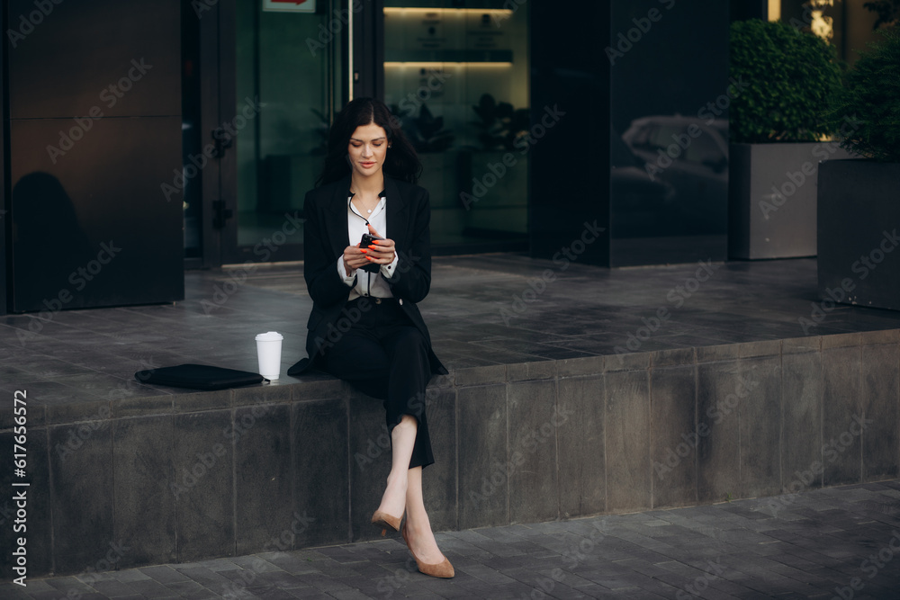 young business woman goes and uses mobile phone in her hands a urban background a modern office building. Attractive businesswoman or student Female walks the city street outdoors using a smartphone.
