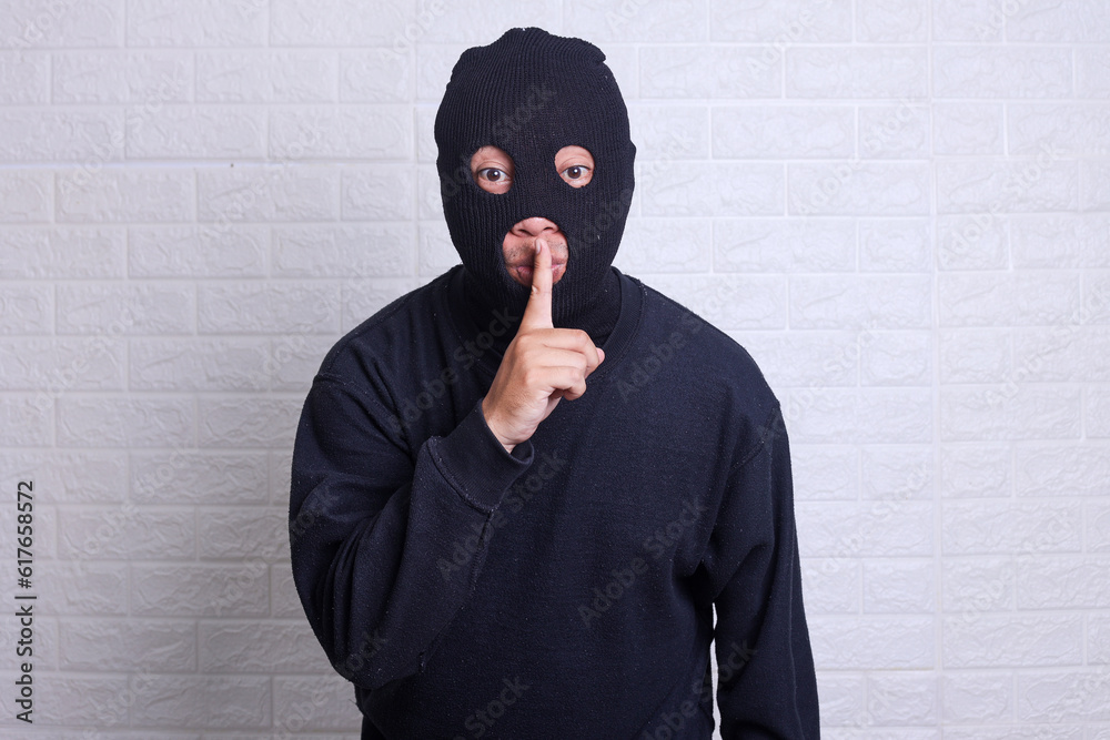 Thief in a mask showing sign quieter isolated on white background Thief in a mask showing sign quieter isolated on white background