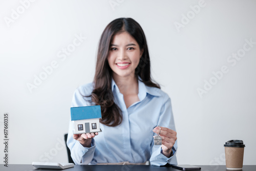 Close up Asian women's hand saving a coin into piggy bank with wooden house model on the table for business, finance, saving money and property investment concept. © Treerat