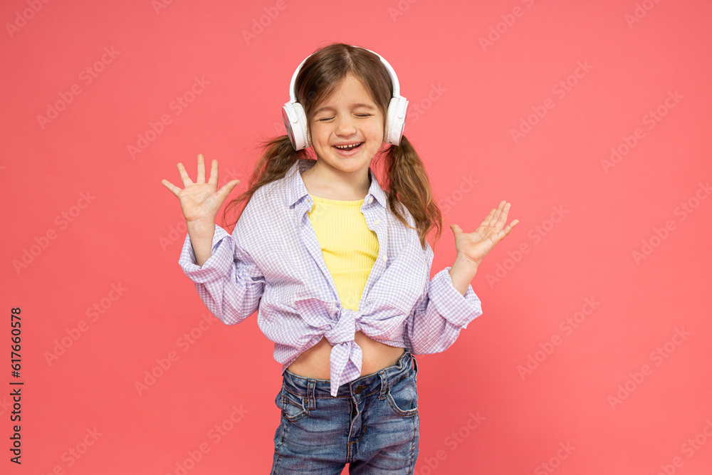 A little girl in headphones on a pink background listens to music. A little girl in headphones on a pink background listens to music.