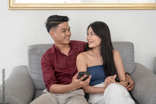 A young asian couple looking at each other fondly after watching a video on a phone. Relaxing on the couch at their condo apartment unit.