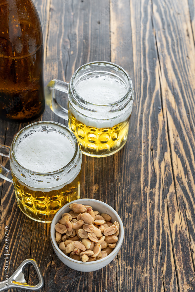 Zwei Biergläser, eine braune Flasche und gesalzene Erdnüsse in einer Schüssel auf einem rustikalen Holz Tisch. Zwei Biergläser, eine braune Flasche und gesalzene Erdnüsse in einer Schüssel auf einem rustikalen Holz Tisch.