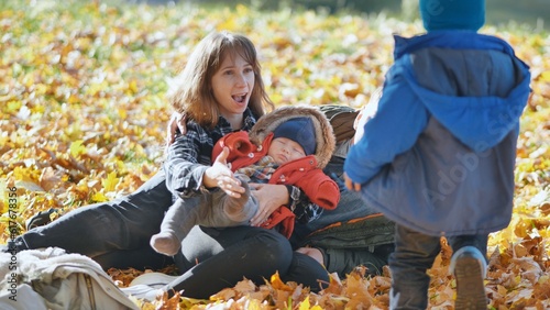 A family and their children enjoy the golden fall in the park sitting on the leaves.
