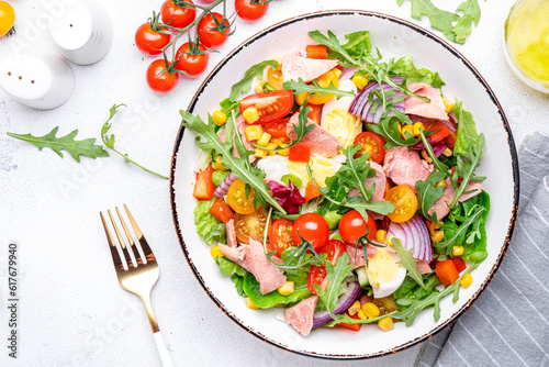 Fresh tuna and vegetable salad bowl with cherry tomatoes, onion, sweet corn, red paprika, lettuce and arugula. White  table background, top view