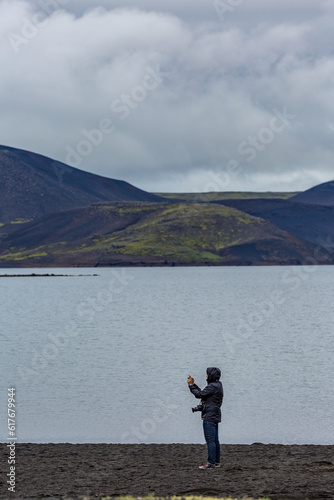 Unrecognizable young female tourist taking photos with her phone, lake, Southern Iceland