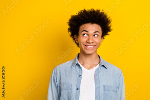 Photo of dreamy funky young man wear jeans shirt looking empty space smiling isolated yellow color background