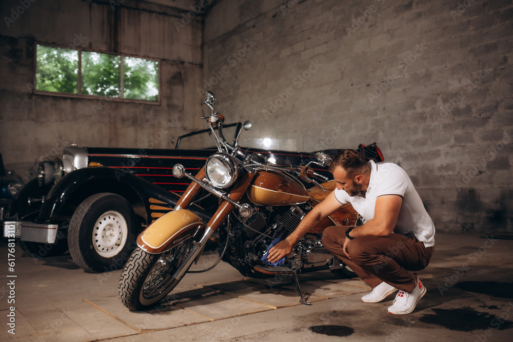 A man wipes the engine of a retro motorcycle. Retro collector of cars and motorcycles - obrazy, fototapety, plakaty 
