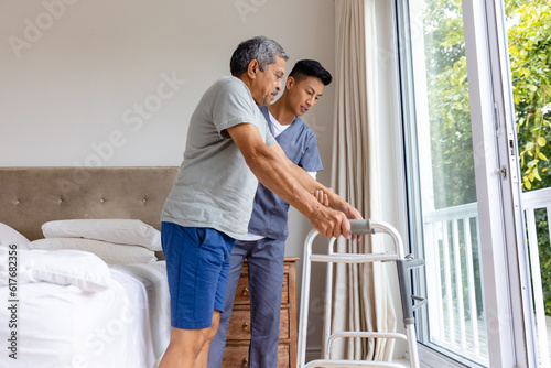Diverse male doctor advising and senior male patient using crutches at home photo
