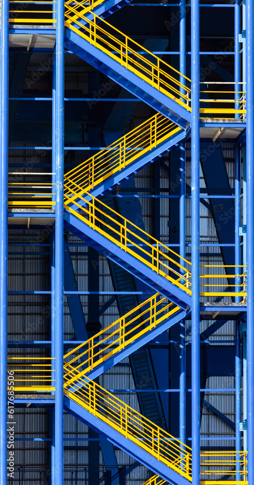 Metal construction fire escape ladder with blue and yellow . .Escape staircase. Fire escape route of a factory. Fire escape stair building. Fire escape staircase on the exterior wall of a warehouse