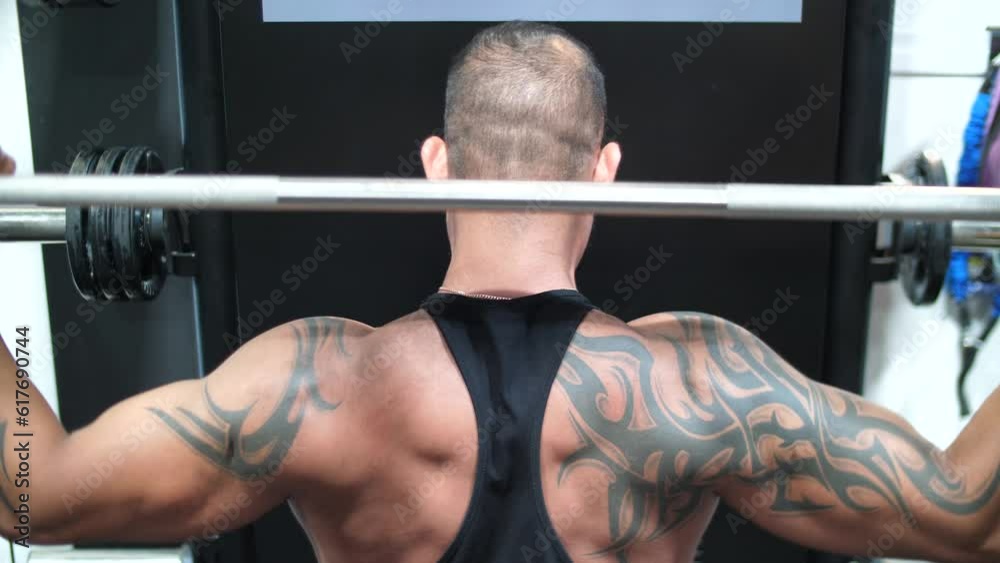 A muscular male bodybuilder lifting weights at the gym from the back A muscular male bodybuilder lifting weights at the gym from the back