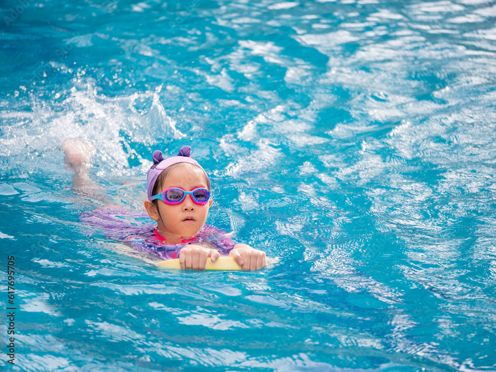 Asian child or kid girl wearing swimming suit to learning on swimming pool , learn and training swim on kick board