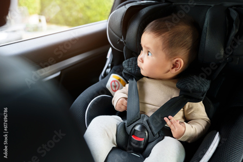 happy infant baby sitting in car seat and looking out of window, safety chair travelling photo