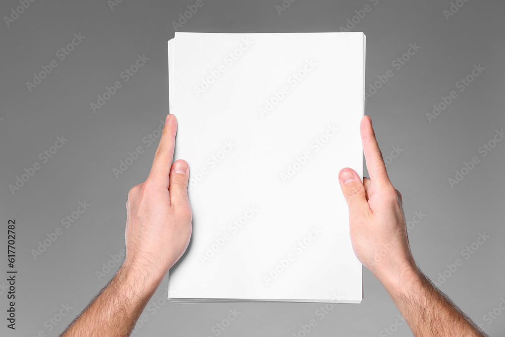 Man holding sheet of paper on grey background, closeup. Mockup for design Man holding sheet of paper on grey background, closeup. Mockup for design