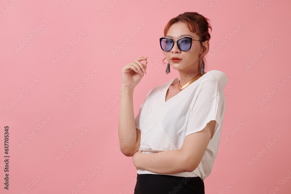 Portrait of stylish transgender woman in sunglasses standing against pink background