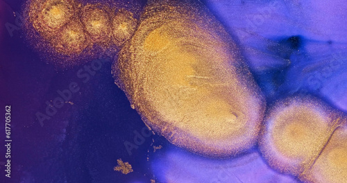 Vertical gold shine on blue-purple ink background. Shiny gold particles in abstract purple liquid. Shining, shimmering golden-blue paint. Acrylic move fluid art. Brilliant wallpaper