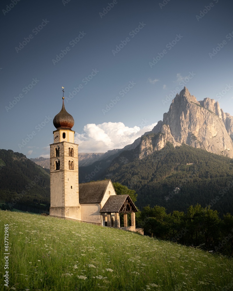 Picturesque small chapel with a bell tower surrounded by lush green grass and mountains