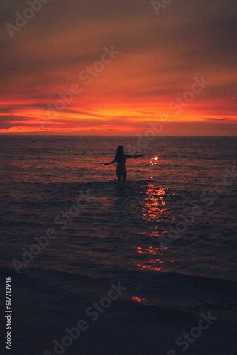 Woman stands in a body of water, illuminated by the soft orange and yellow hues of the setting sun © 趙堯/Wirestock Creators