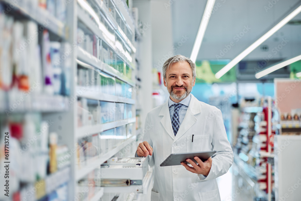 Portrait of a grey-bearded smiling male pharmacy employee with a tablet.