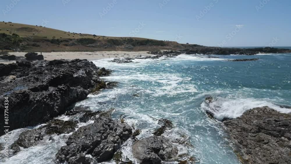 Aerial of the foamy sea waves hitting the rocks and the sandy shore in Otago, New Zealand Aerial of the foamy sea waves hitting the rocks and the sandy shore in Otago, New Zealand