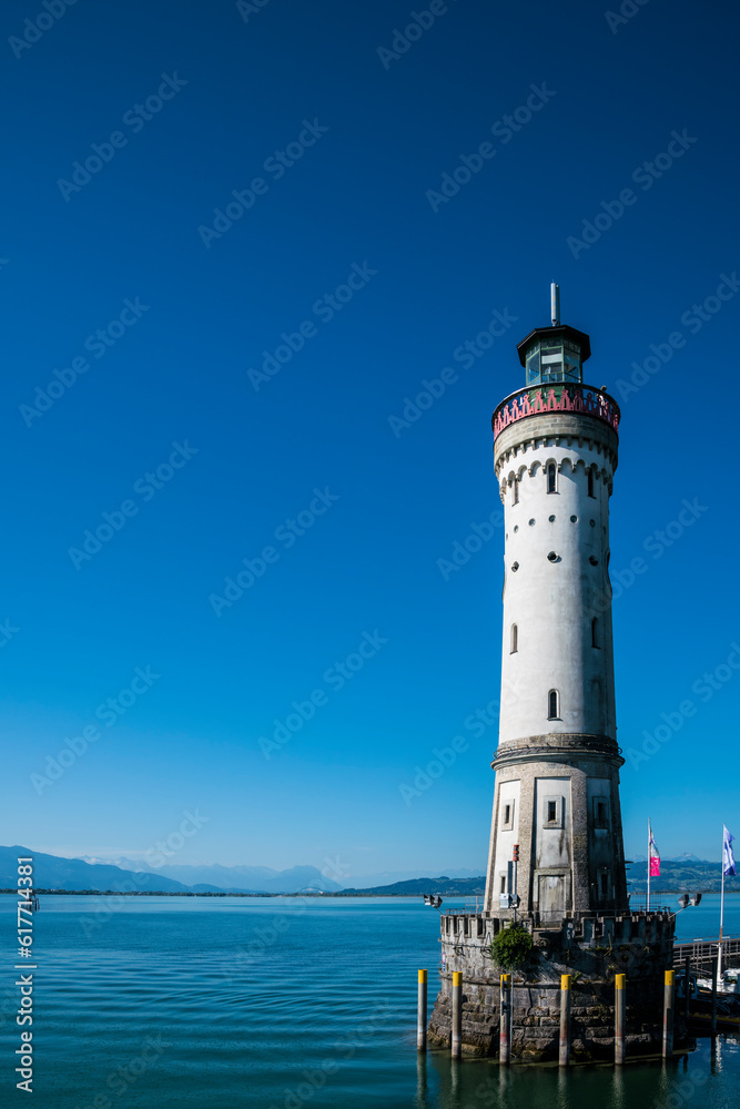 Germany, Lindau harbour lighthouse and beautiful view to austrian alps mountains, early morning after sunrise, silent water and blue sky