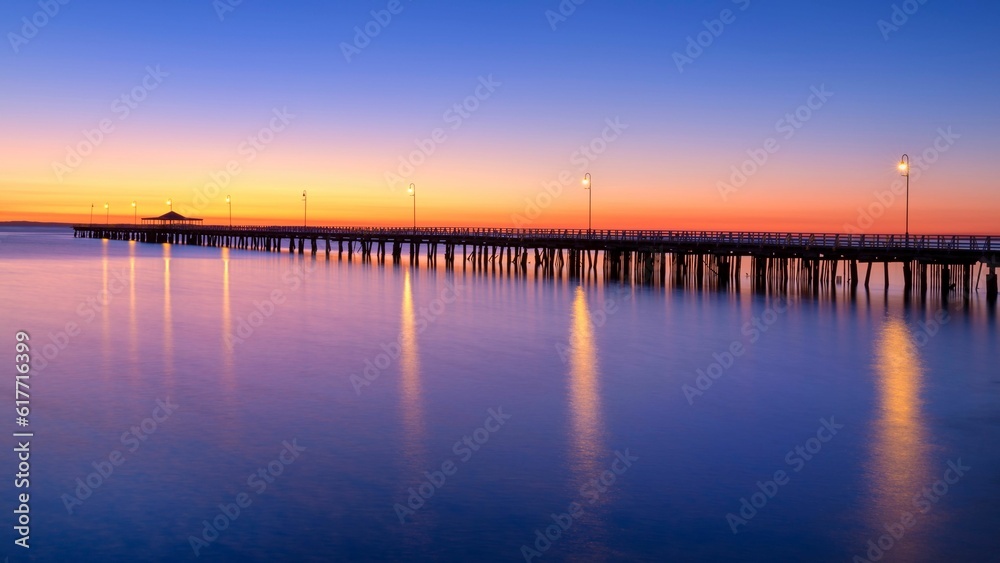 a pier is lit up at night by the water's edge