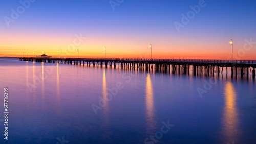 a pier is lit up at night by the water's edge © Danwnz/Wirestock Creators
