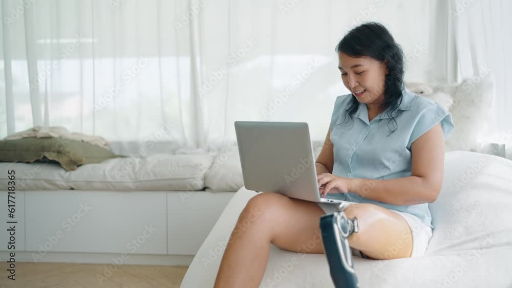 Happy asian woman in prosthetic leg using laptop notebook typing message, chatting on browsing surfing internet social media or working online at home. Leg prosthetic equipment, Amputee concept Happy asian woman in prosthetic leg using laptop notebook typing message, chatting on browsing surfing internet social media or working online at home. Leg prosthetic equipment, Amputee concept