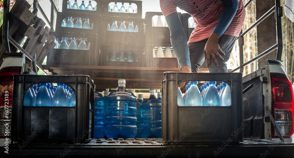 Workers lift blue drinking water bottles in crates into the back of a ...