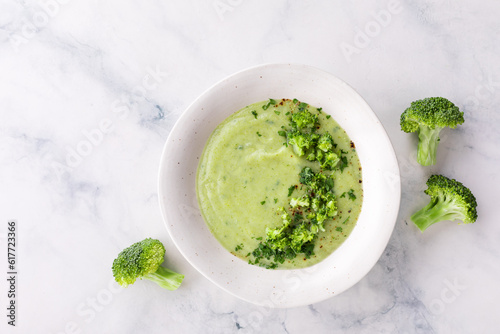 Homemade broccoli cream soup with green parsley in white bowl on stone table top view. Healthy vegan dish.