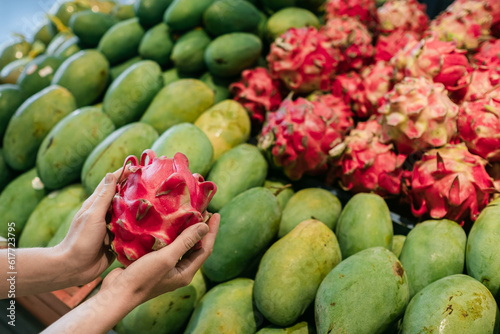 Photography Female hands close-up, holding a dragon fruit against the background of a fruit stand, in a supermarket