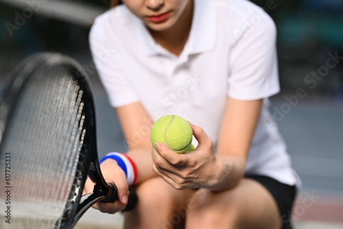 Pensive young female tennis player holding ball racket sitting on the bench at tennis court © Prathankarnpap