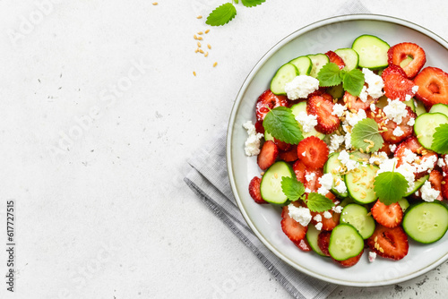 Healthy cucumber strawberry feta cheese salad with honey lemon dressing on plate. Top view, flat lay, copy space.