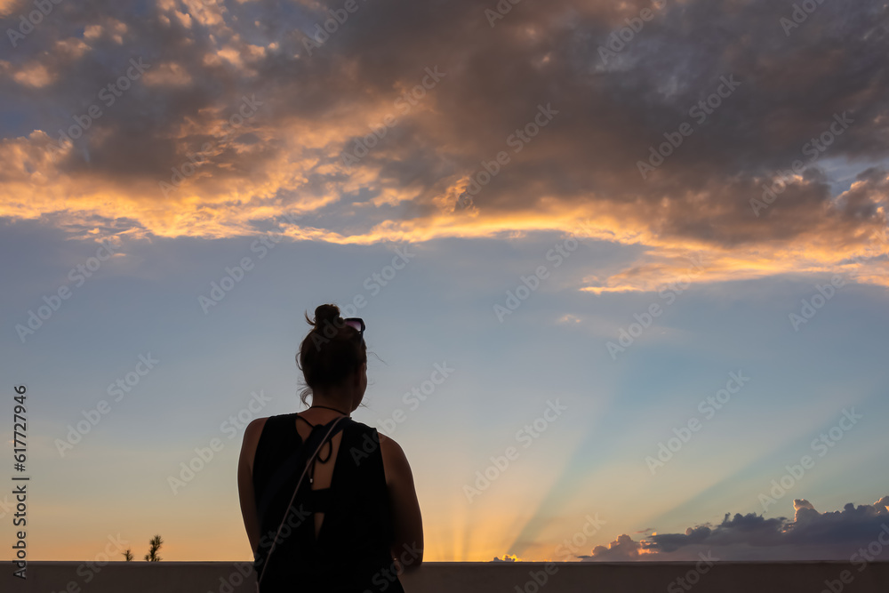 Fototapeta premium Rear view of silhouette of woman that gazes at the colorful horizon as the sun sets in Las Vegas, Nevada, USA. Clouds turn red and orange during the golden hour. Romantic atmosphere. Serenity