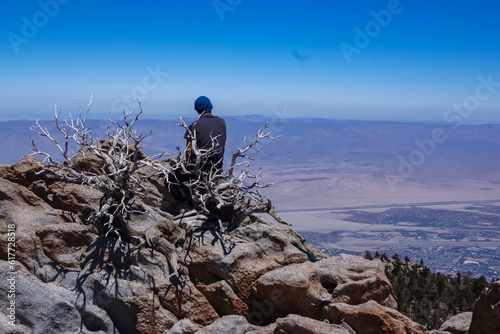Rear view of man with scenic aerial vistas of Coachella Valley seen from the top of Palm Springs tramway station in Mt. San Jacinto State Park, California, USA. Mountain landscape. Trees in foreground
